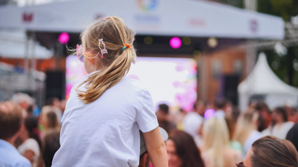 Little girl with ponytail enjoying latin american festival with crowd watching live music concert