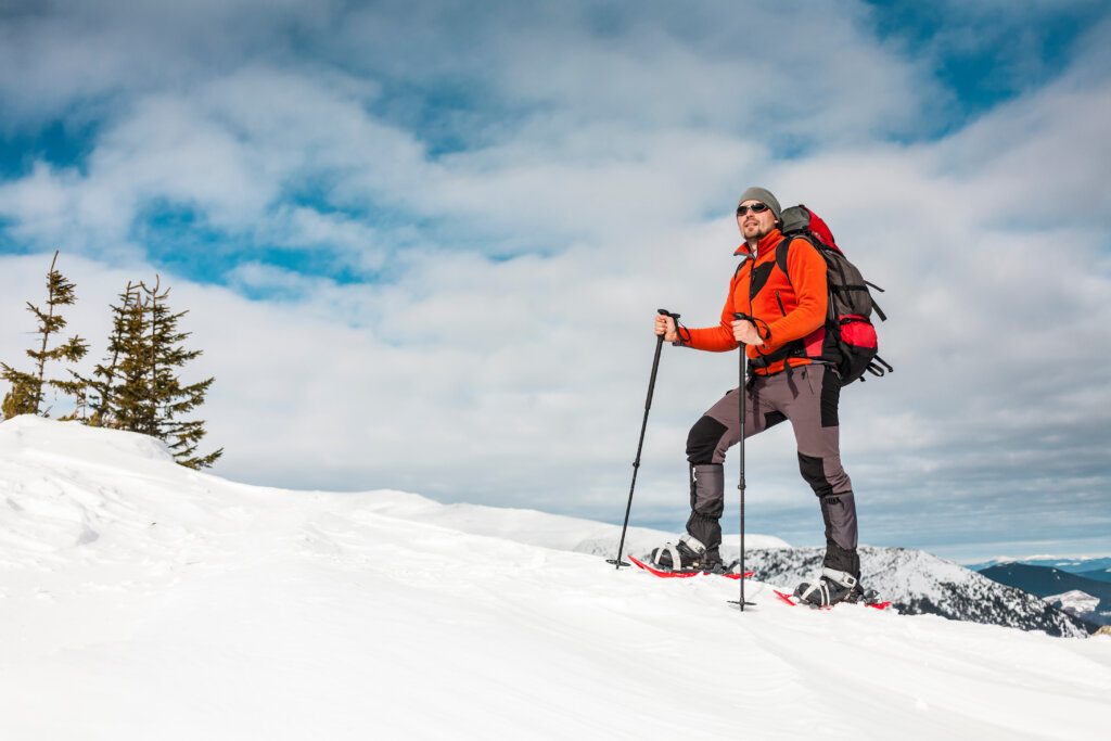 Winter climbing the mountain. A man in snowshoes is climbing to the top. Winter ascent. A mountaineer with a backpack and trekking sticks. Equipment for winter hiking.