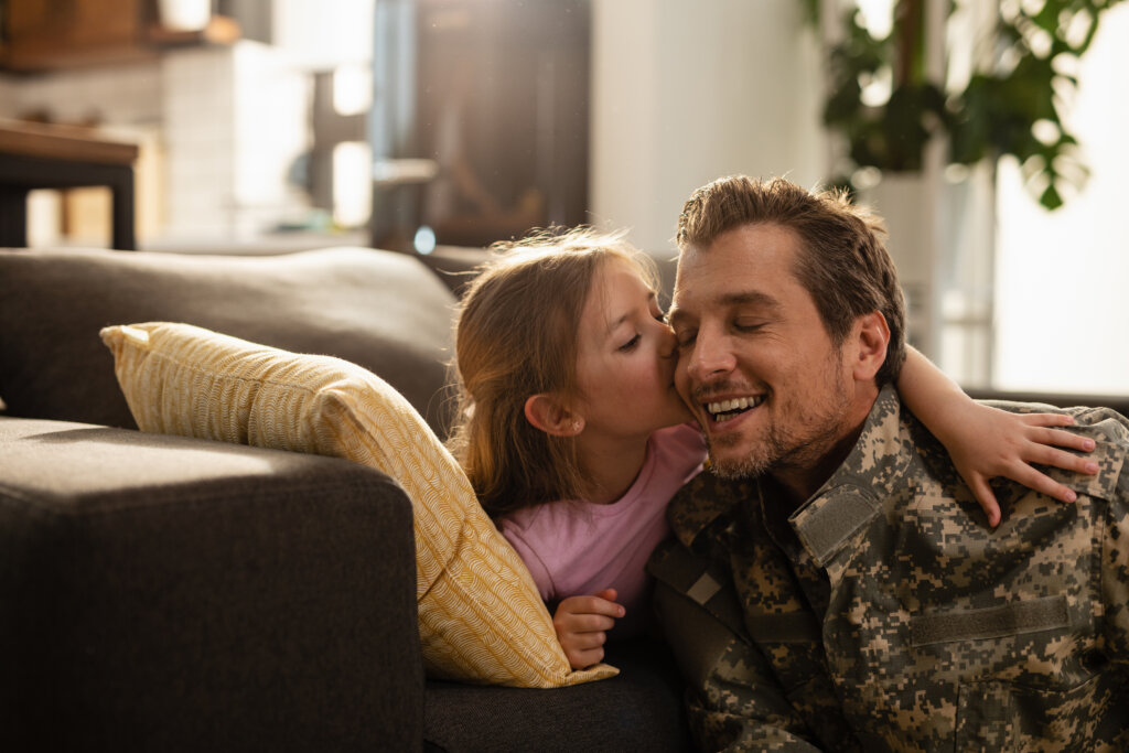 Loving daughter kissing her military father on the cheek while reuniting at home.