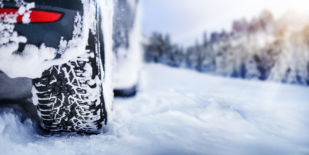 Winter tire panorama detail in snowy mauntains. Car tires in snow with sun lights in background.