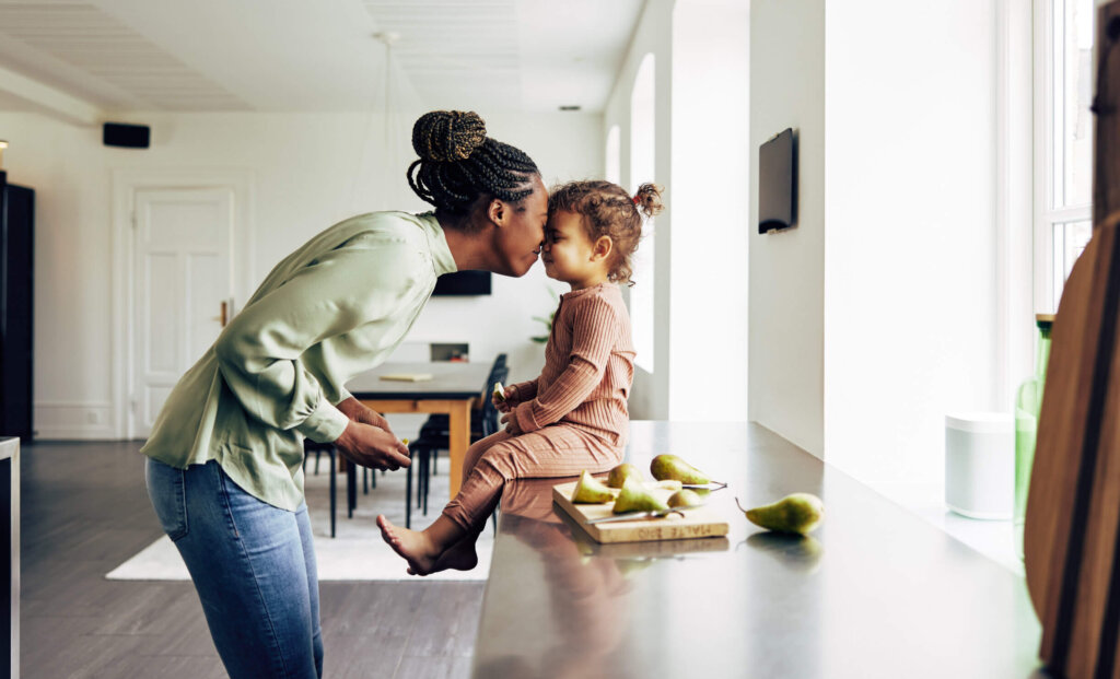 Loving young African mom and her cute little daughter eating a healthy fruit snack together in their kitchen at home