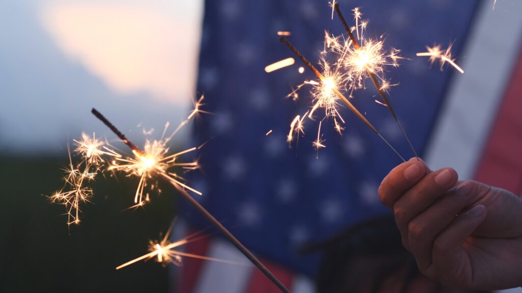 Happy 4th of July Independence Day, Hand holding Sparkler fireworks USA celebration with American flag background. Concept of Fourth of July, Independence Day, Fireworks, Sparkler, Memorial, Veterans