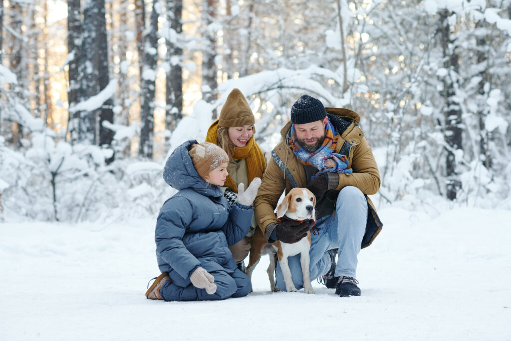 Family of three walking with dog in winter forest 