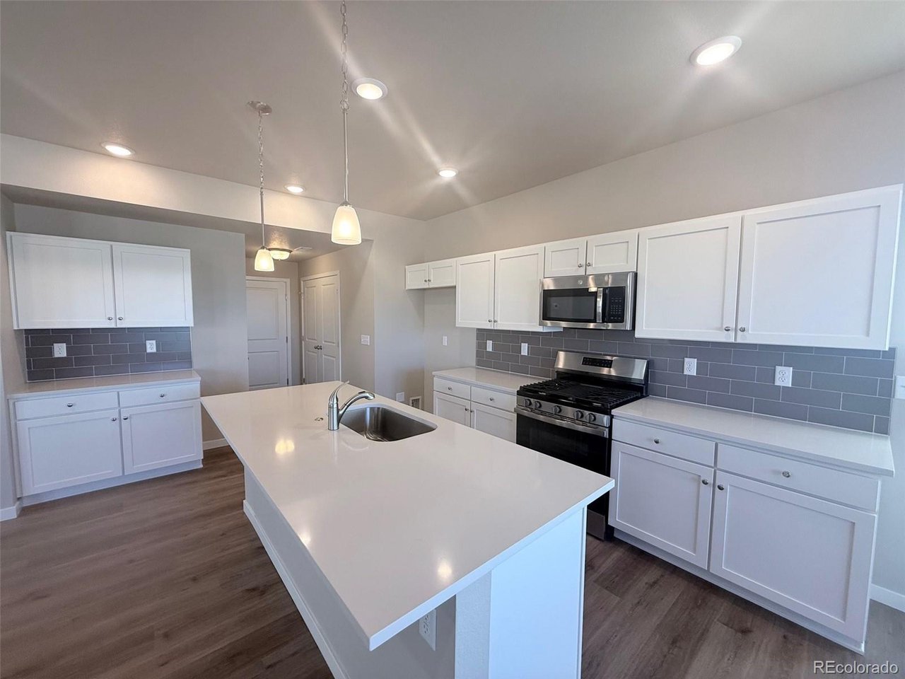 kitchen with large island, white shaker cabinets, gray subway tile backsplash, stainless steel range and microwave, pendant lights